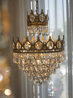 Clérachic crystal chandelier glowing in front of sheer curtains, with soft bokeh lights behind its copper-toned crown tiers.