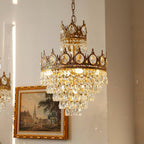 Low angle on this Clérachic chandelier's crown tiers and crystal drops, next to a gilt-framed painting on a warm wall.