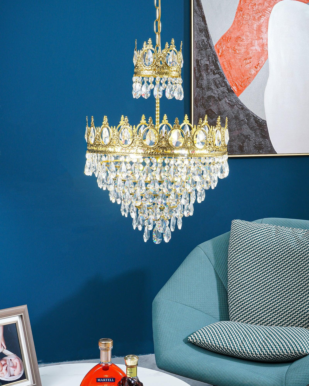 Clérachic crystal chandelier hung against a deep blue wall with an abstract print, a teal armchair below.