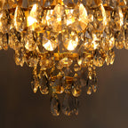 Close view of the lit clear crystal drops and tiered rings on this Clérachic chandelier, glowing amber against a dark wall.