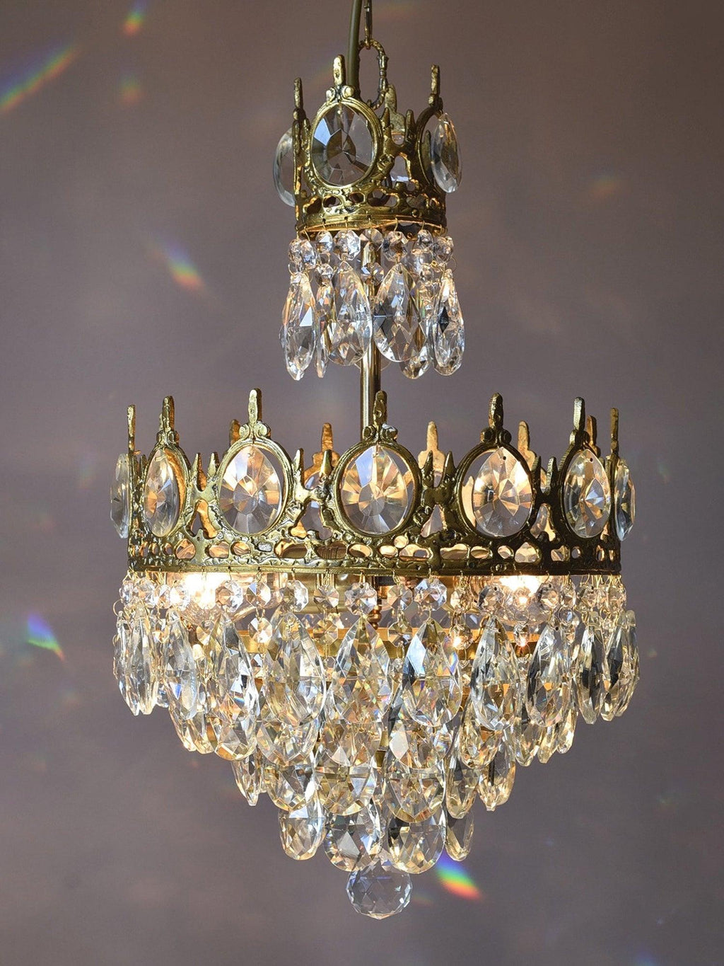 Clérachic crystal chandelier against a mauve backdrop, with small rainbow reflections from the crystal drops.