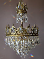 Unlit Clérachic chandelier against a mauve backdrop, showing its crown-edged tier and the clear teardrop crystals.