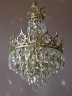 Side view of this Clérachic chandelier on a mauve backdrop, with a small crown tier above a larger tier of crystals.