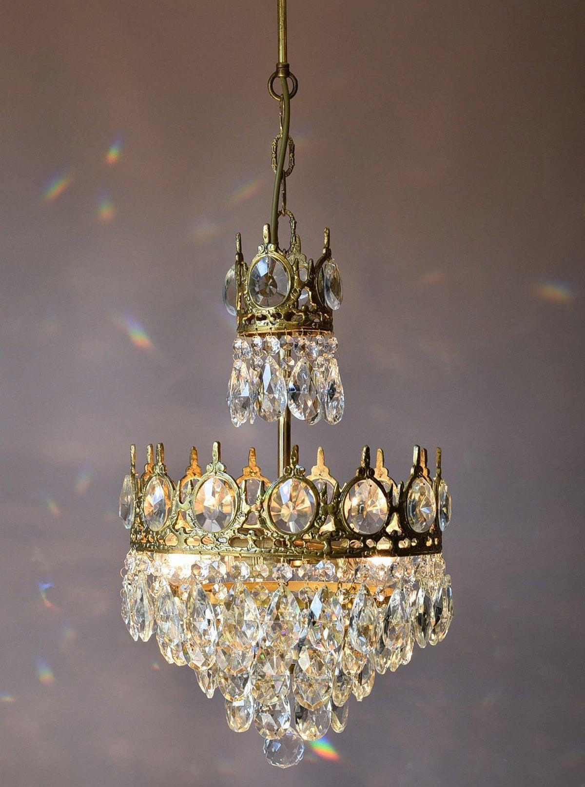 Smaller Clérachic chandelier hung on a chain against a mauve backdrop, with a small crown tier above a short crystal skirt.