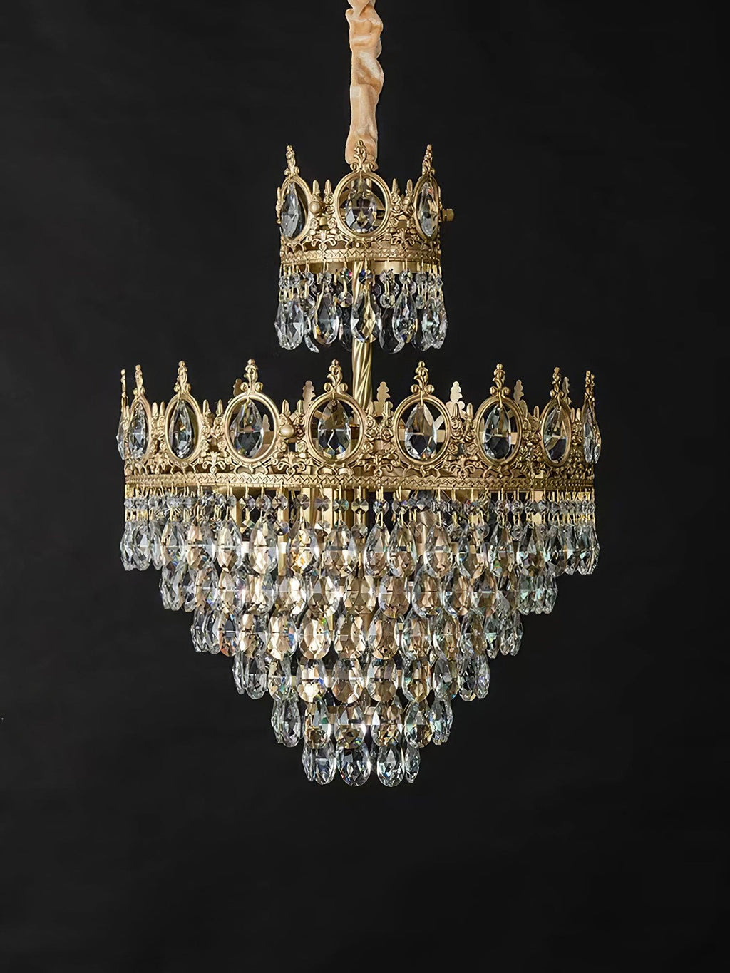 Clérachic crystal chandelier on a black backdrop, with a gold-wrapped chain, a small crown tier and a larger tiered skirt.