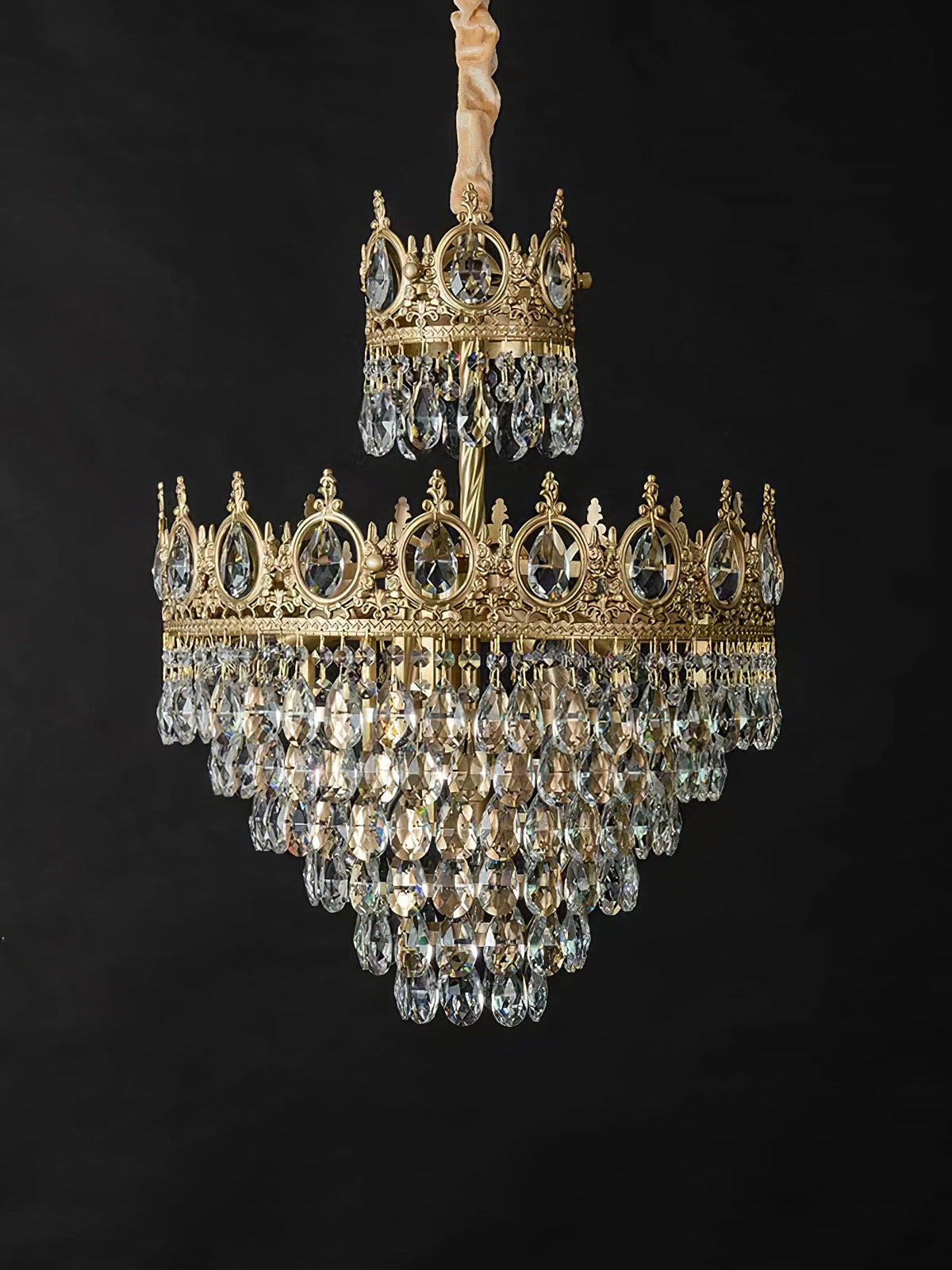 Clérachic crystal chandelier on a black backdrop, with a gold-wrapped chain, a small crown tier and a larger tiered skirt.