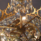 Close view of the lit bulbs in their brass holders, seen from below through the crystal drops of this Clérachic chandelier.