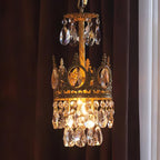 Small Clérachic chandelier glowing amber in front of a dark curtain, its crown ring hung with clear teardrop crystals.