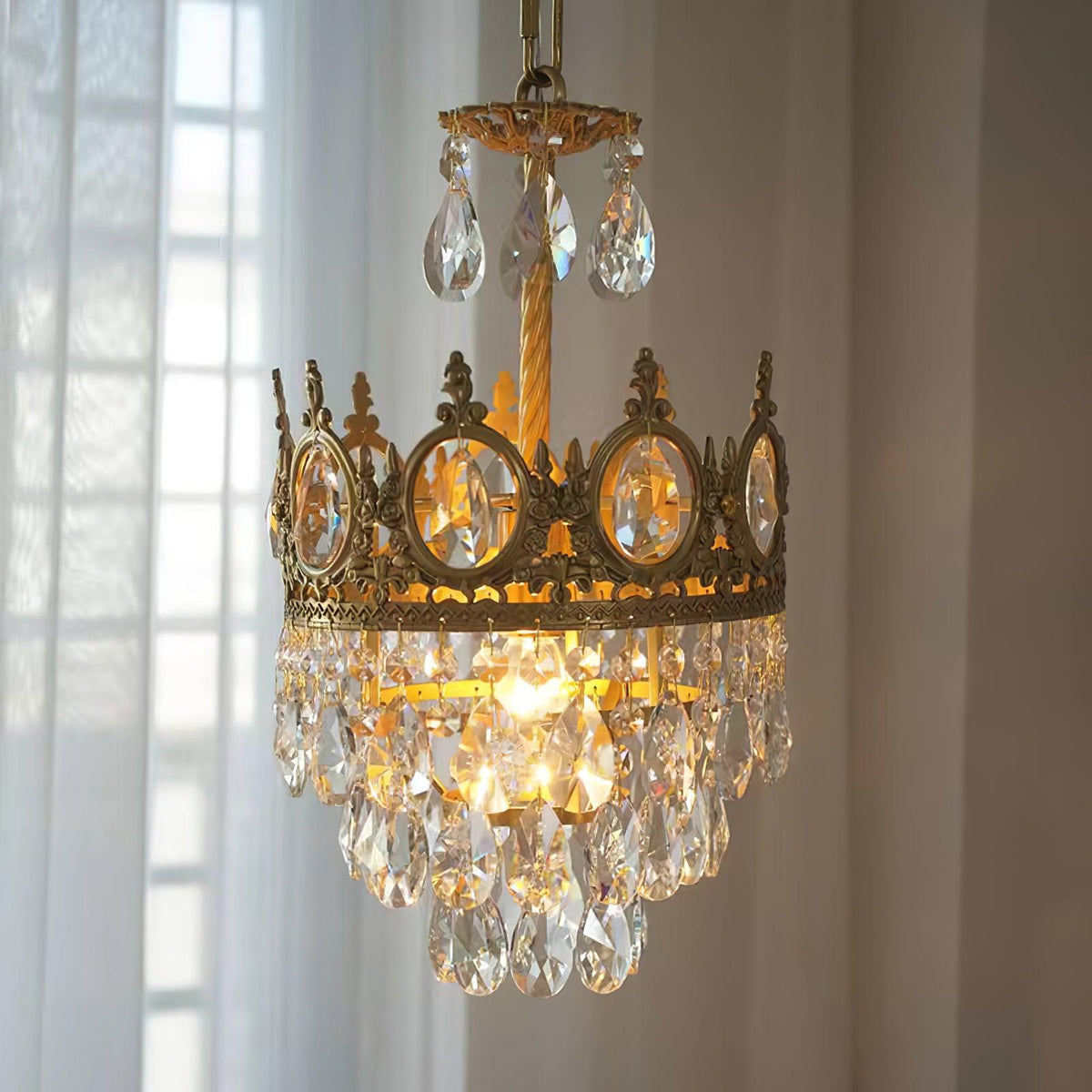 Small Clérachic chandelier lit beside a sheer window curtain, with a crown ring and a skirt of clear crystal drops.