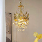 Smaller Clérachic chandelier lit warm against a pale wall, with an arched-corridor print and a yellow leaf at the edge.