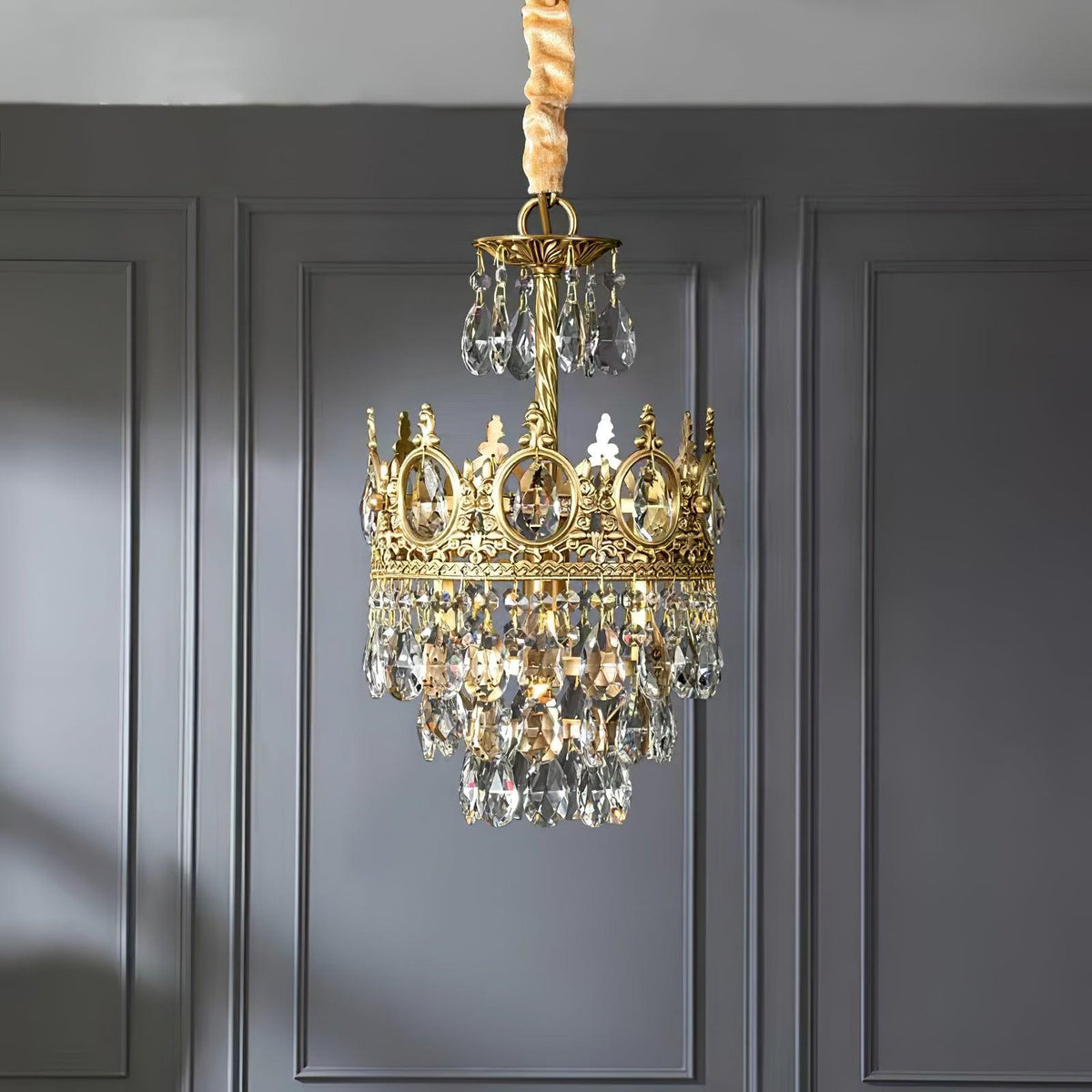 Smaller Clérachic chandelier against a grey panelled wall, with a gold-wrapped chain and a crown ring of clear crystals.