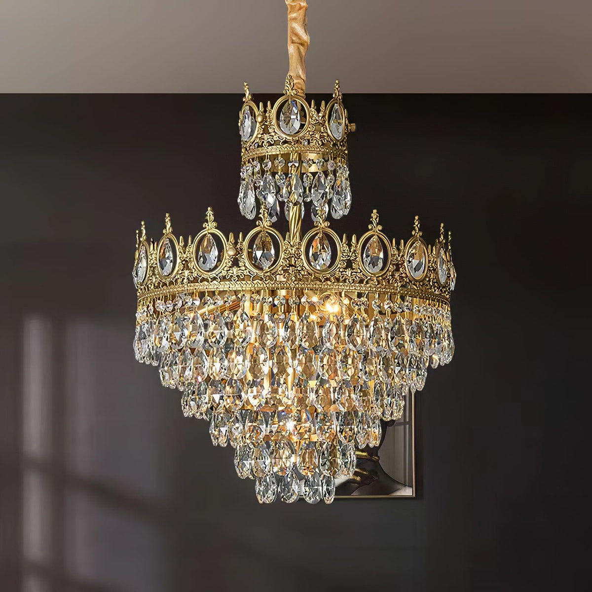 Clérachic crystal chandelier against a dark grey wall, its two crown tiers and layered crystals lit warmly.