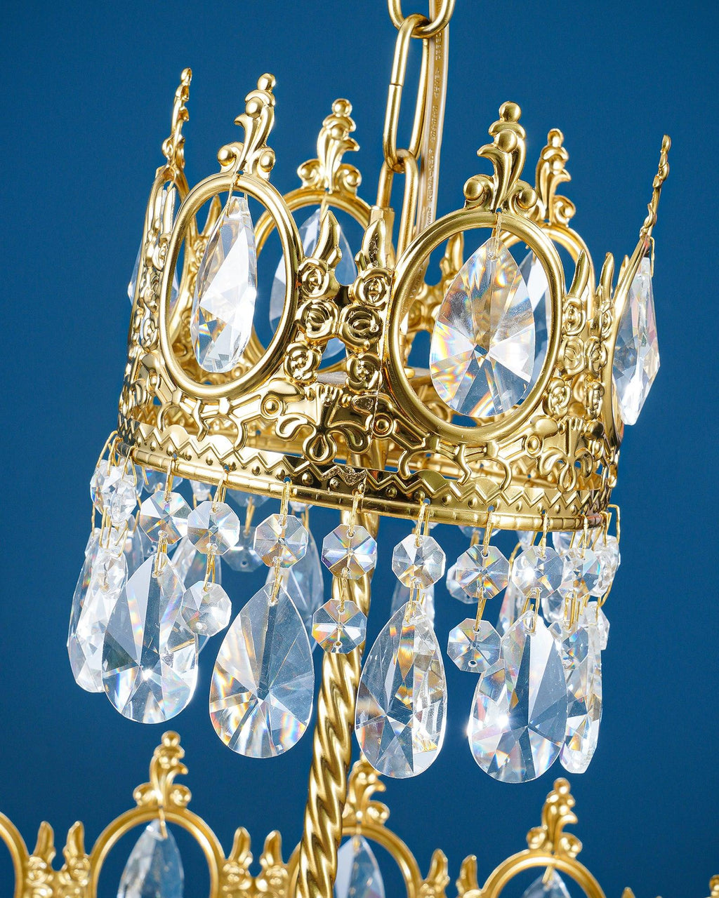 Close view of the gold crown ring with rose motifs and clear teardrop crystals on this Clérachic chandelier, on blue.