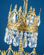 Close view of the gold crown ring with rose motifs and clear teardrop crystals on this Clérachic chandelier, on blue.