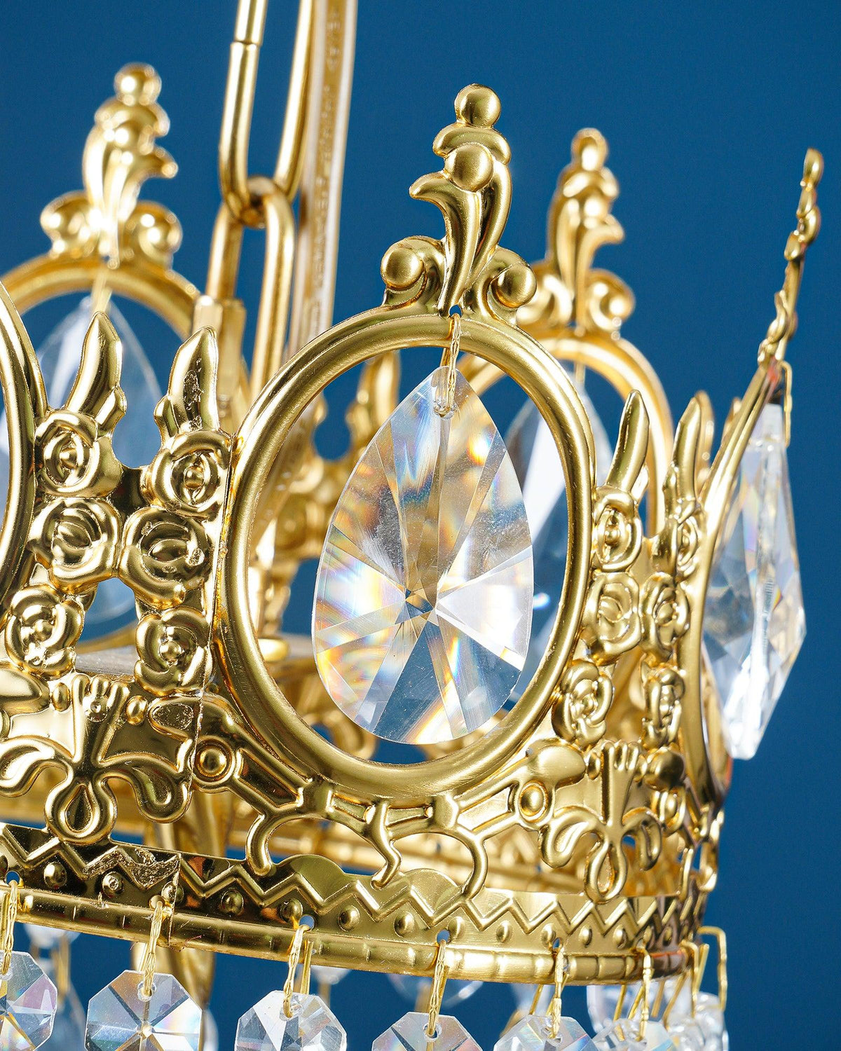 Close view of one cast crown tier with a ring-set crystal and a chain link on this Clérachic chandelier, on blue.