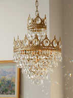 Clérachic crystal chandelier on a pale wall, with a corner of a gilt-framed painting and rainbow light flecks.