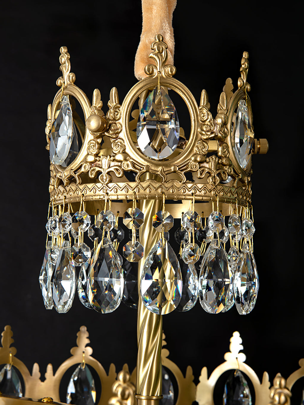 Close view of the crown ring, twisted brass stem and teardrop crystals of this Clérachic chandelier, on black.