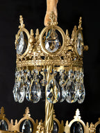 Close view of the crown ring, twisted brass stem and teardrop crystals of this Clérachic chandelier, on black.