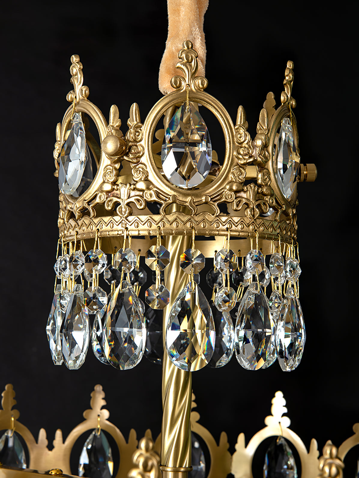 Close view of the crown ring, twisted brass stem and teardrop crystals of this Clérachic chandelier, on black.