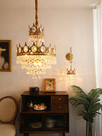 Clérachic chandelier lit in a small room with a framed portrait, a crown-shaped wall light and a dark sideboard.