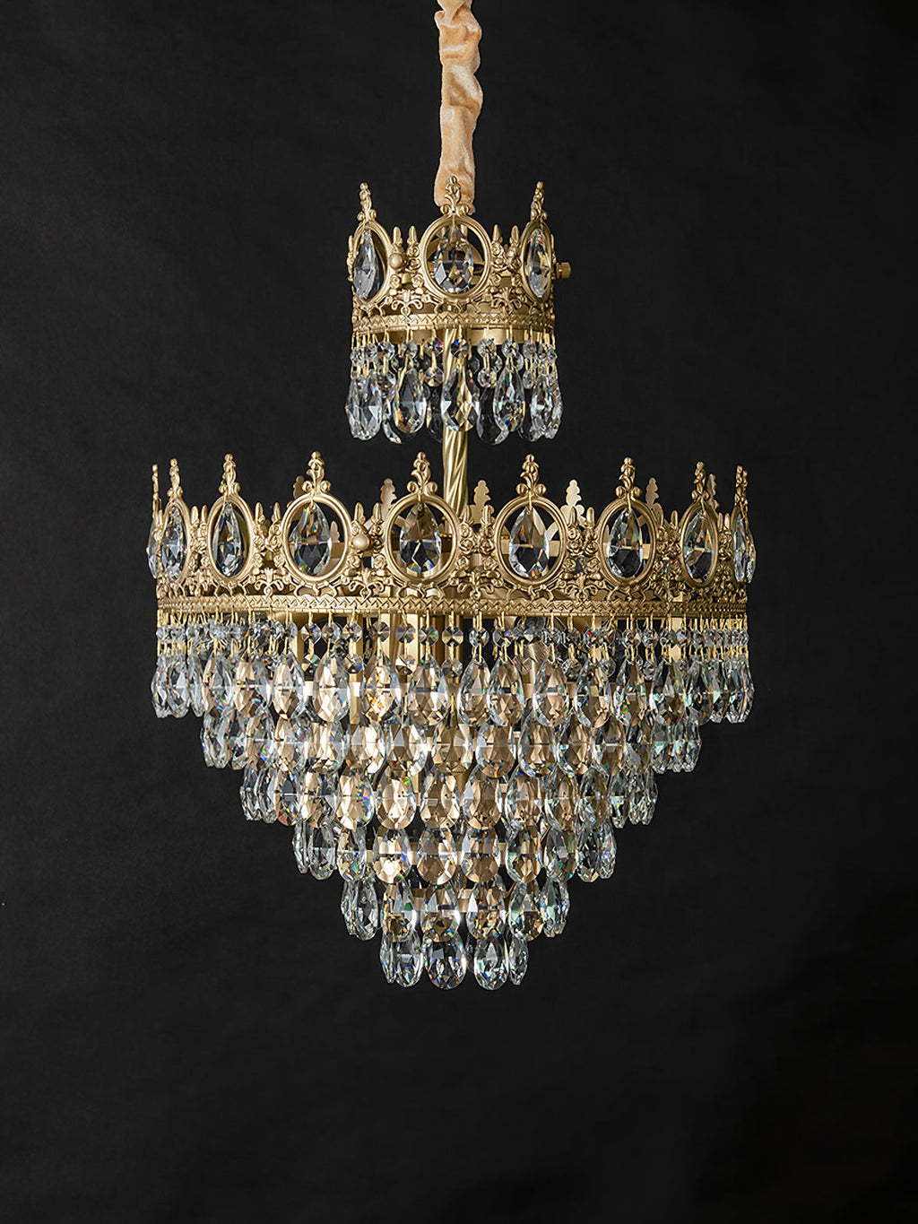 Clérachic crystal chandelier on a black backdrop, with a gold-wrapped chain and two crown tiers of clear drops.