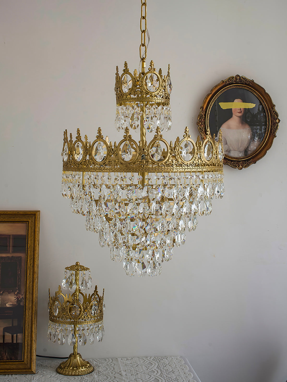 Clérachic crystal chandelier on a white wall with an oval portrait, above a small crown-shaped table lamp.