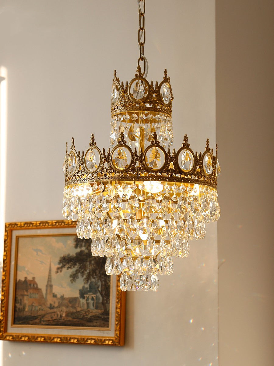 Clérachic crystal chandelier hung on a chain beside a gilt-framed painting of a village street, on a cream wall.