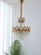 Clérachic crystal chandelier hung from a gold-wrapped chain, with white curtains and a palm frond below.