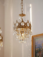 Smaller Clérachic chandelier on a chain, next to a gilt-framed palm painting on a warm cream wall.