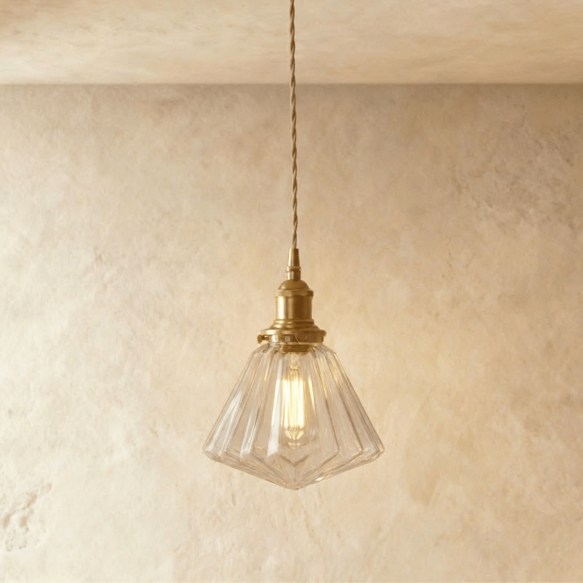 Clérachic Isabel pendant light, a faceted geometric clear glass cone shade catching light on angled brass fitting.