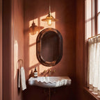 A Clérachic Isabel pendant light hangs above a marble sink in a warm terracotta powder room beside an oval mirror.