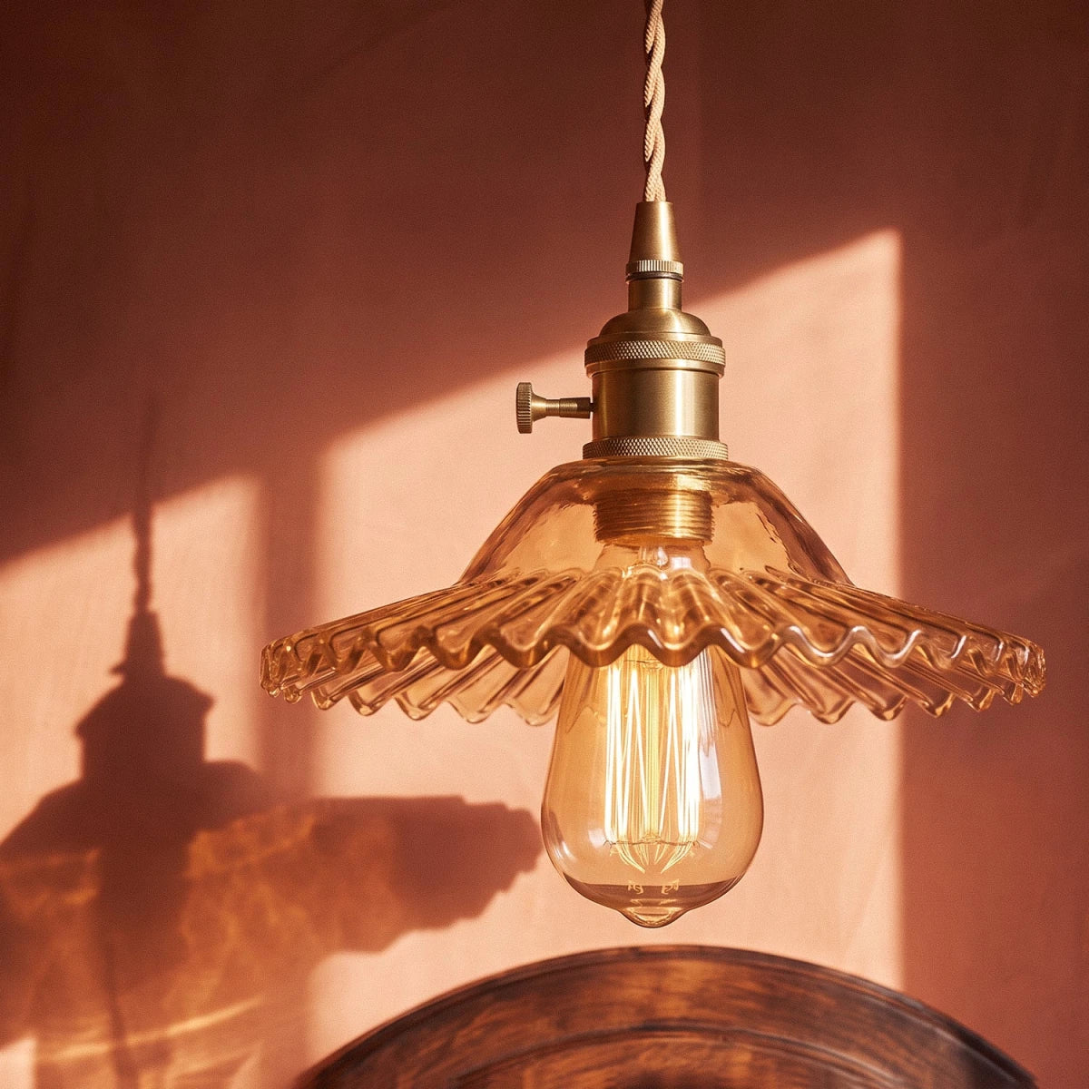 Close-up of a Clérachic Isabel pendant light's amber ribbed scalloped shade, sunset light catching its exposed bulb.