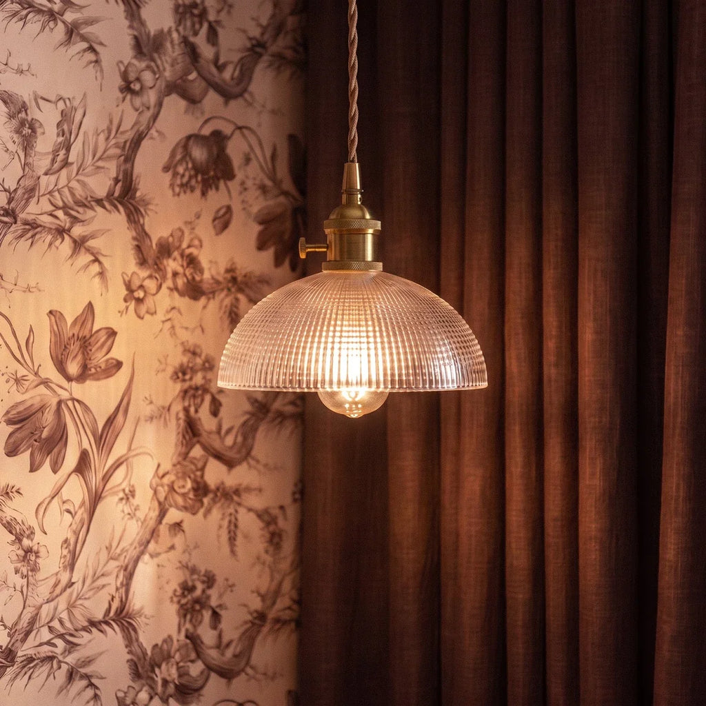 A Clérachic Isabel pendant light with a woven grid glass shade hangs against dark curtains and floral toile wallpaper.
