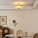 Lit Clérachic pleated ceiling light above a dining room, with a marble-topped round table, a silver teapot and a cane-fronted cabinet.