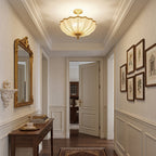 A Clérachic ceiling light in a panelled hallway with a gilt-framed mirror, a dark wood console and a gallery of botanical prints.