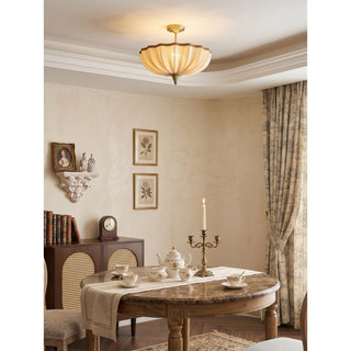 Clérachic pleated ceiling light above an oval wooden dining table set with a teapot and a brass candelabra, beside floral curtains.