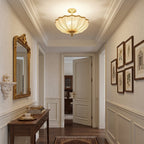 Seen from the far end of a hallway, a Clérachic ceiling light hangs above a console table, a gilt mirror and a row of framed prints.