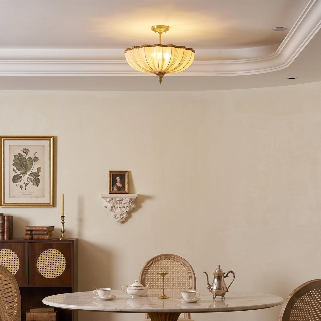 A lit Clérachic ceiling light over a corner of a cream dining room, with a framed botanical print and a small portrait on a shelf.