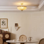 A lit Clérachic ceiling light over a corner of a cream dining room, with a framed botanical print and a small portrait on a shelf.