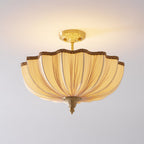 Front view of the lit Clérachic ceiling light, its pleated cream fabric glowing warm beneath a brass ceiling plate.