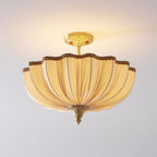 The Clérachic ceiling light lit, a scalloped fabric edge with a braided trim and a brass finial at the base.