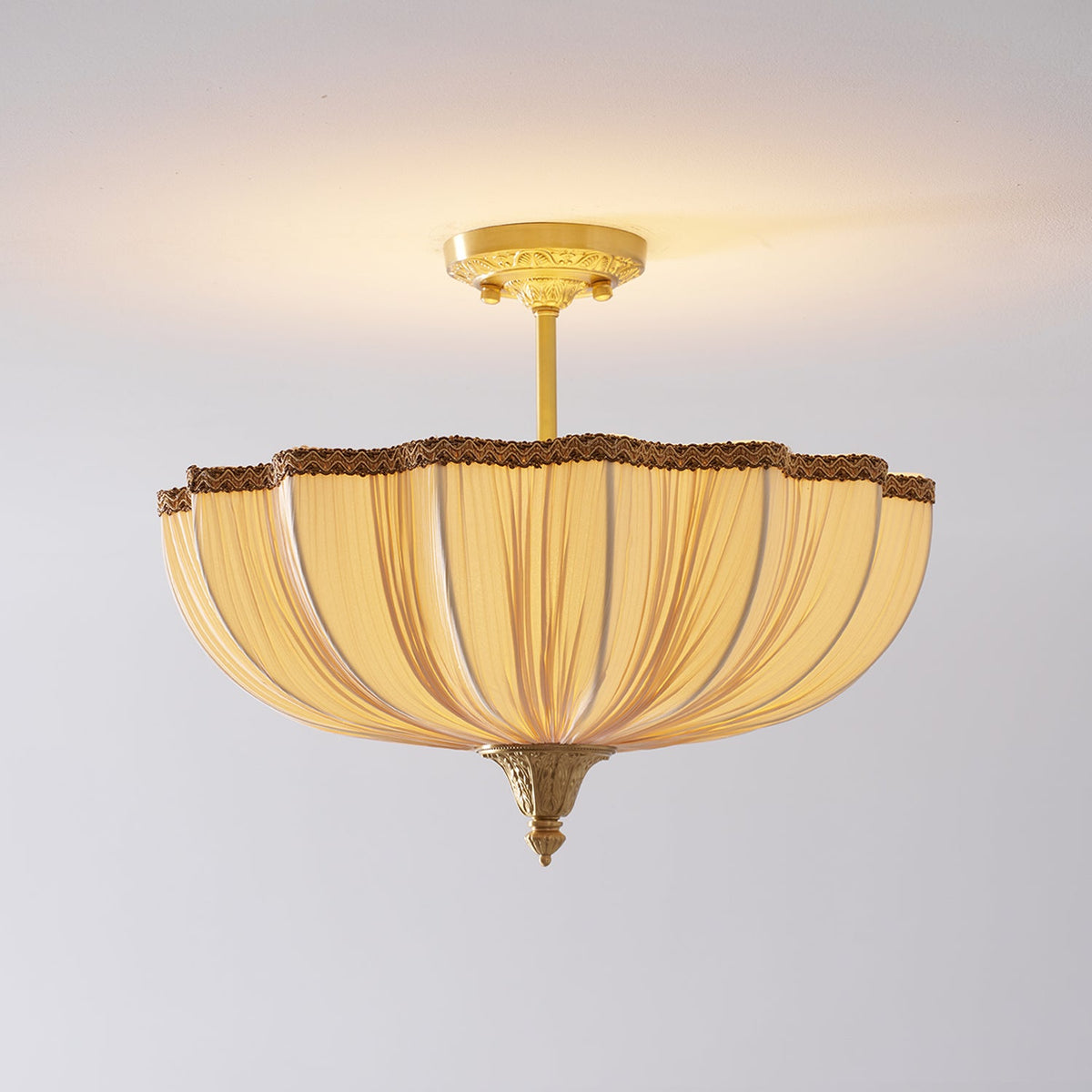 The Clérachic ceiling light lit on a pale ceiling, with a longer view of its brass stem and a warm glow above the shade.