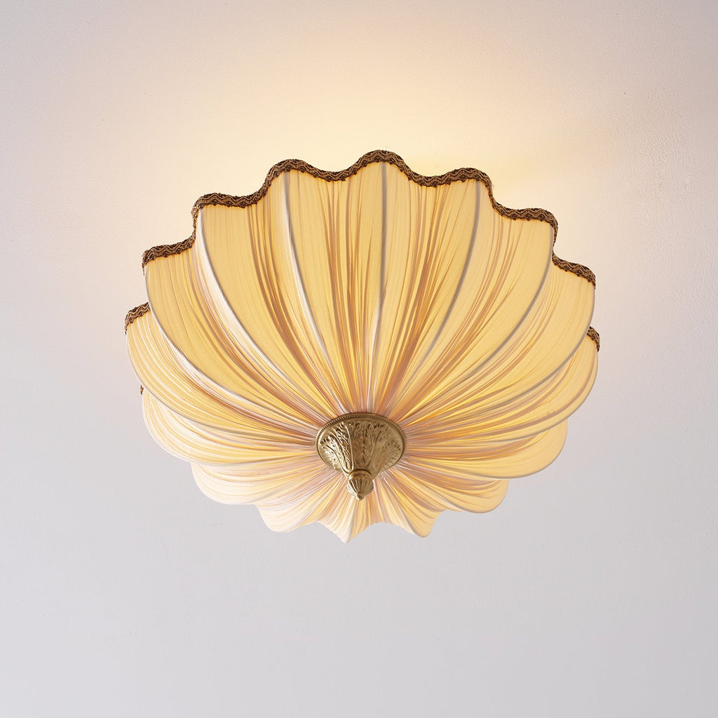 Clérachic ceiling light from a low angle, lit, showing the underside of the pleated shade fanning out from its brass finial.