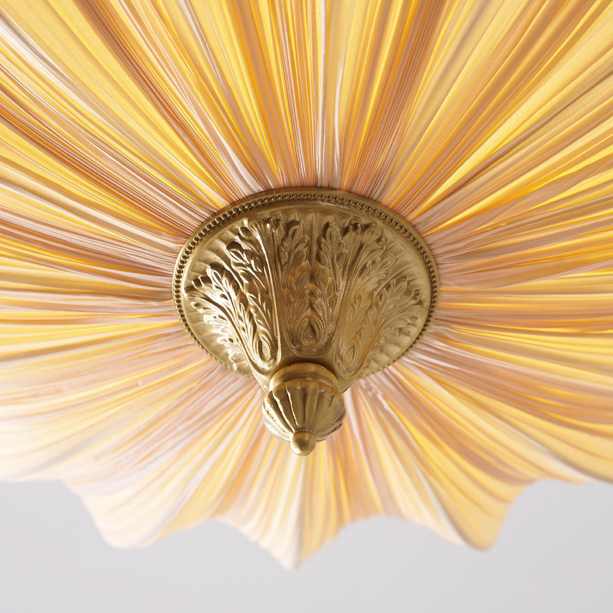 Close view up into the base of the Clérachic ceiling light, with a carved brass finial where the pleats meet.