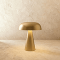 Clérachic gold table lamp with a rounded dome shade and tapered cone base, lit softly against a limewash wall.