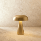 Clérachic gold table lamp with a rounded dome shade and tapered cone base, lit softly against a limewash wall.