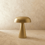 Clérachic gold table lamp, its brushed dome shade glowing warm, stands centred on a limewash backdrop.