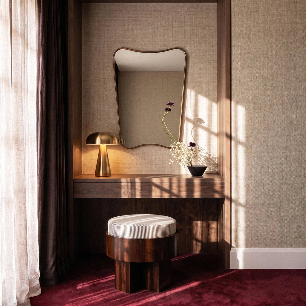 Clérachic gold table lamp lit on a walnut vanity beneath a curved mirror, with fresh flowers nearby.