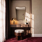 Clérachic gold table lamp lit on a walnut vanity beneath a curved mirror, with fresh flowers nearby.