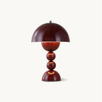 A wine red Clérachic table lamp with a dome shade over a base of stacked spheres, on a plain off-white backdrop.